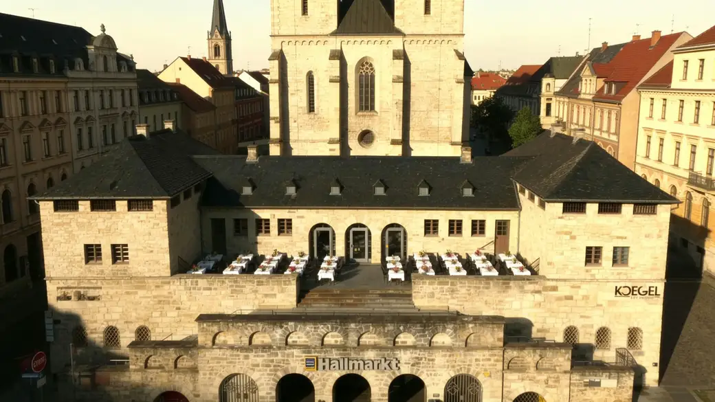 Das historische Umspannwerk in der Altstadt von Halle (Saale) mit eingedeckten Tischen vor den Sandstein-Arkaden – Visualisierung